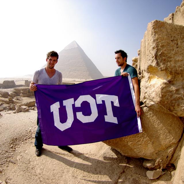 两名男学生手持本校校旗靠近金字塔